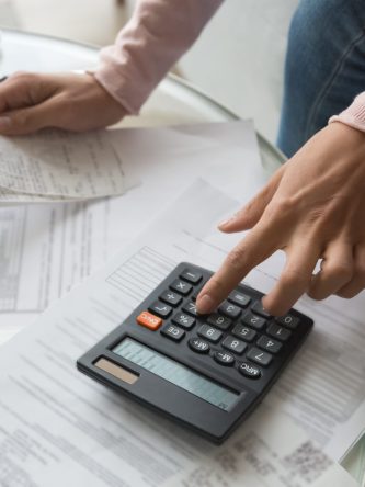 Close up cropped image coffee table full with papers invoices cheque bills, female hands holding receipt calculating company expenses results of incomes, bookkeeper accountant doing paperwork concept