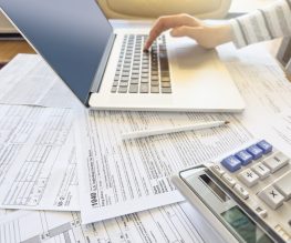 Close up photo of a woman doing taxes with laptop and tax forms in a house